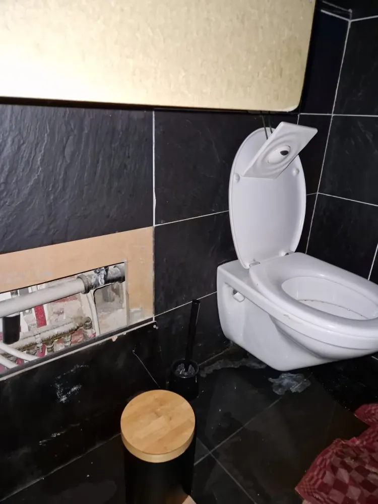 Toilette suspendue ouverte révélant des tuyauteries et une trappe de maintenance.